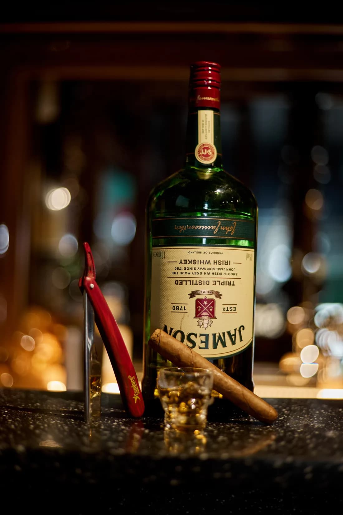 An open cut-throat razor beside a bottle of whiskey and a cigar on the bar
